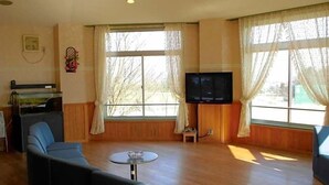A living room with a sofa, a television, and large windows with curtains. - Oyabe City Cycling Terminal (Oyabe)
