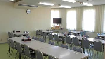 A classroom with multiple tables and chairs, a clock on the wall, and a television on a stand.