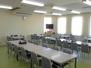 A classroom with multiple tables and chairs, a clock on the wall, and a television on a stand. - Oyabe City Cycling Terminal (Oyabe)