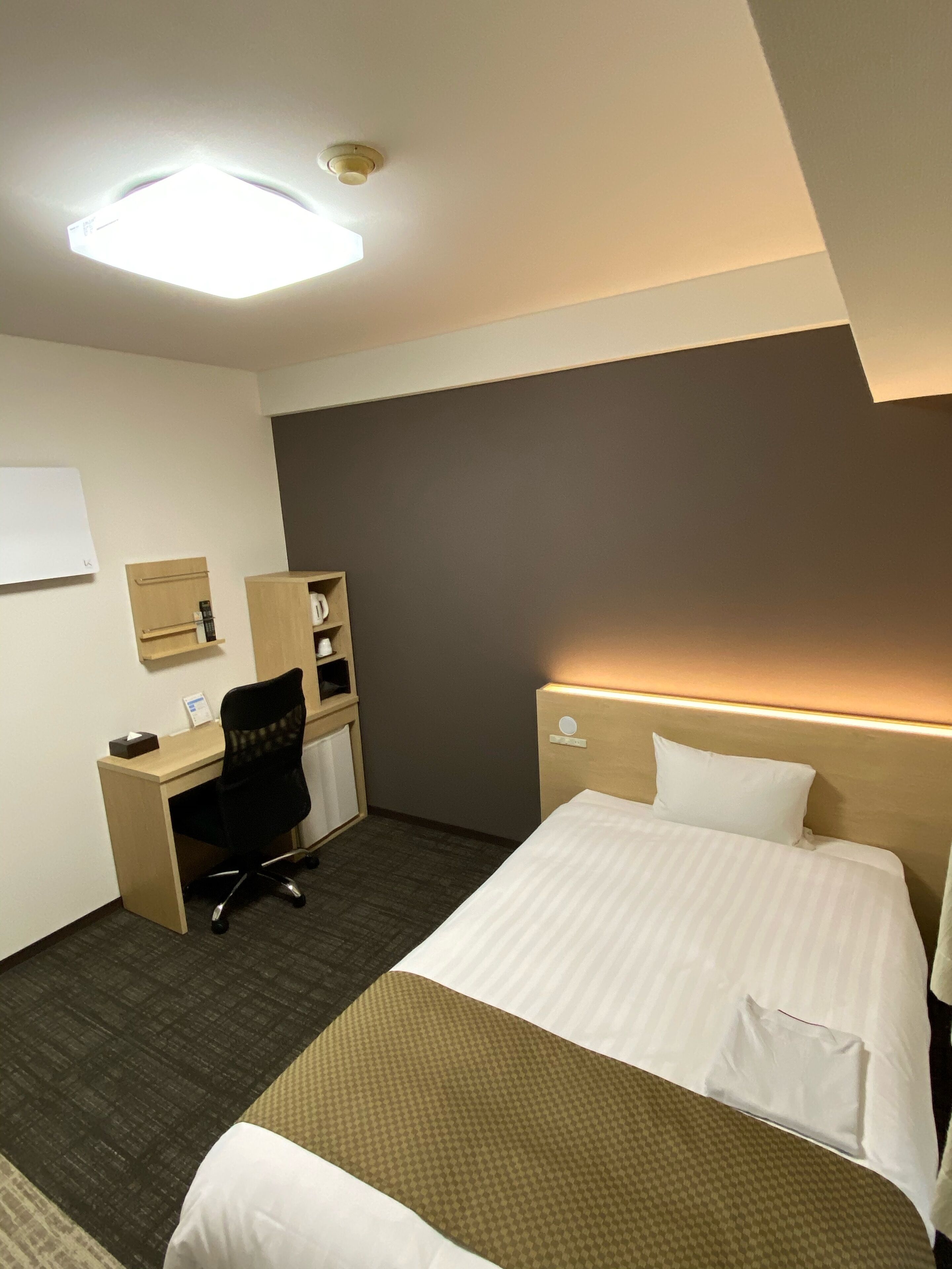 A hotel room with a bed, desk, chair, and a small cabinet.