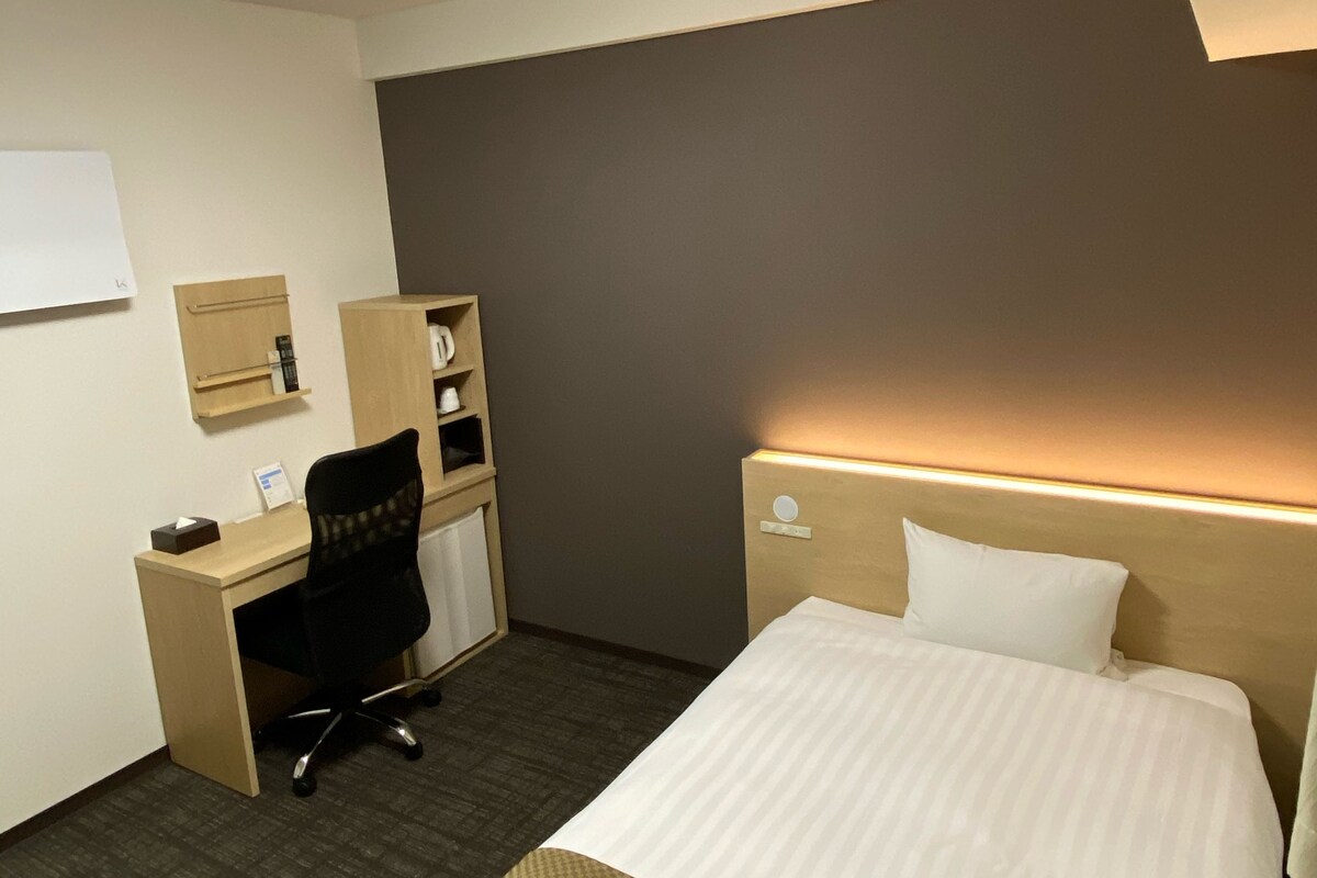 Ein Hotelzimmer mit Bett, Schreibtisch, Stuhl und einem kleinen Schrank.