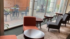 Ett rum med ett stort fönster, en sittgrupp med orange och grå stolar och ett litet runt bord.