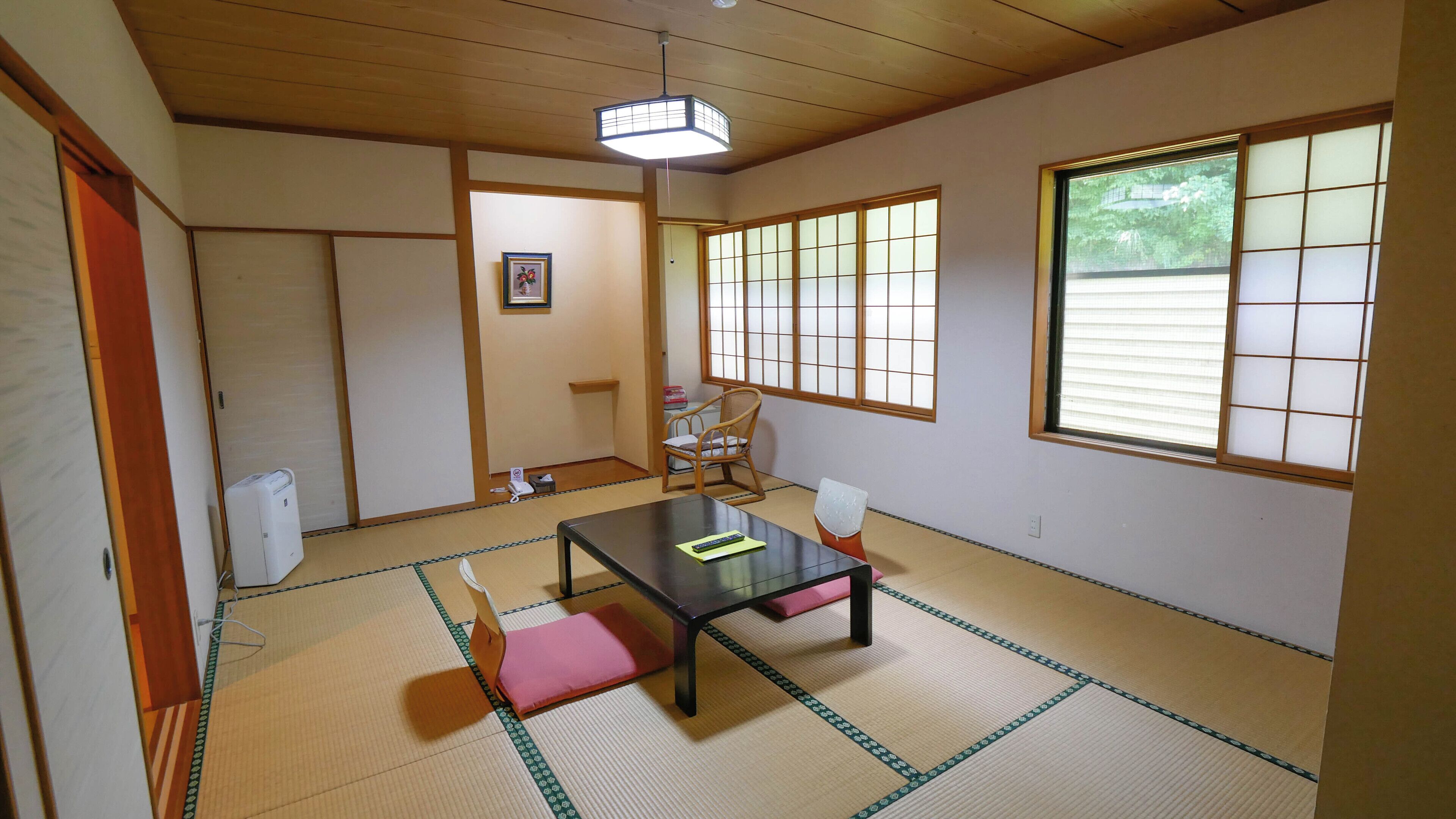 A traditional Japanese room with tatami flooring, a low table, a chair, a window with shoji screens, and a ceiling fan.