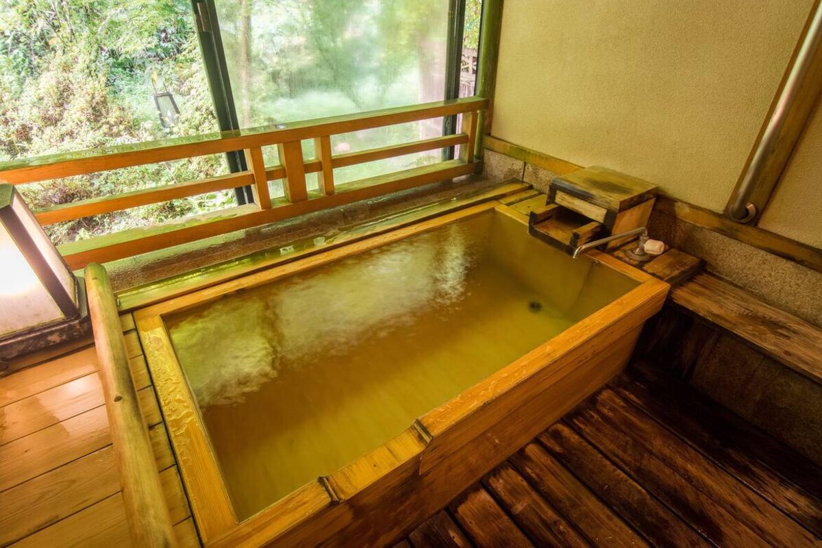 Una vasca termale in legno con una panca di legno e una finestra con vista sul verde.