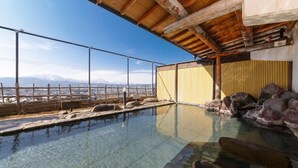 A clear view of a swimming pool with a wooden deck and rocks, a wooden ceiling, and a view of distant mountains.