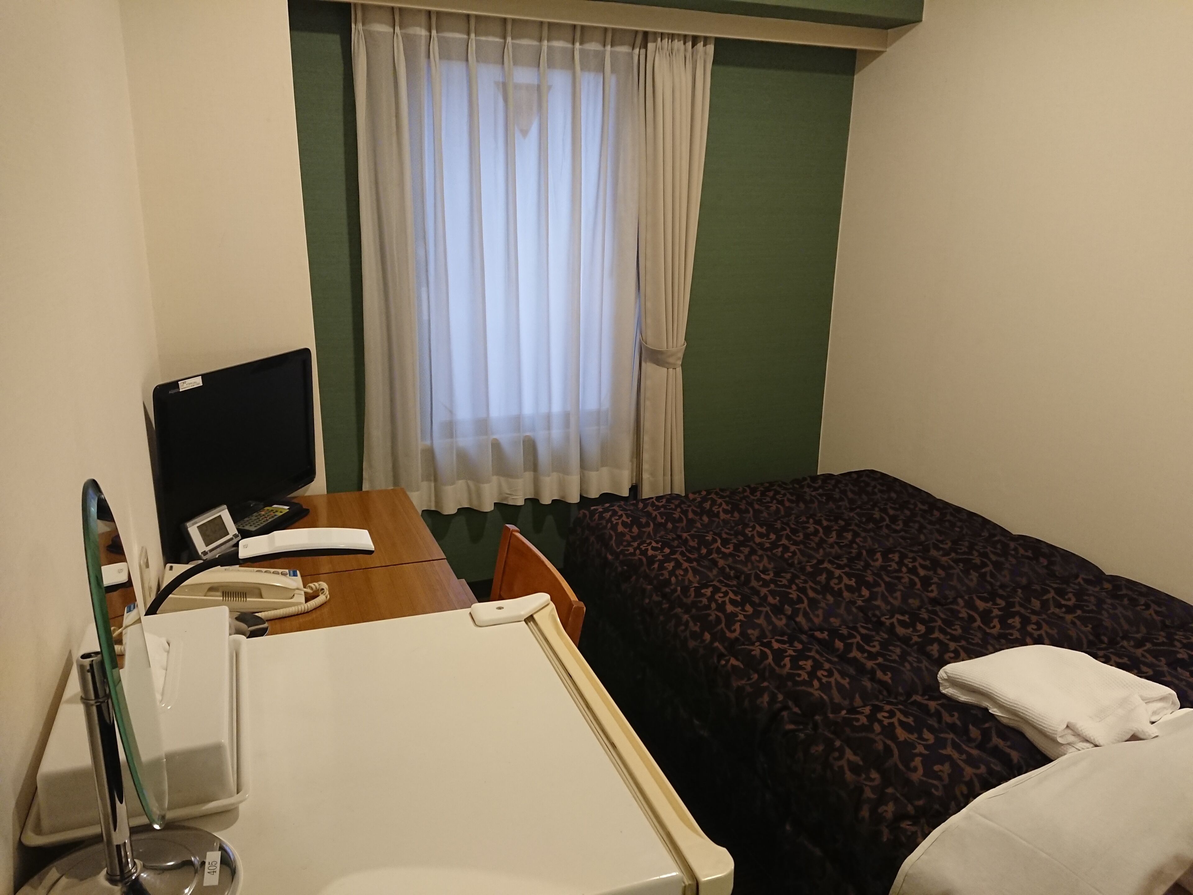 A hotel room with a bed, a desk with a computer, a telephone, and a bedside table.
