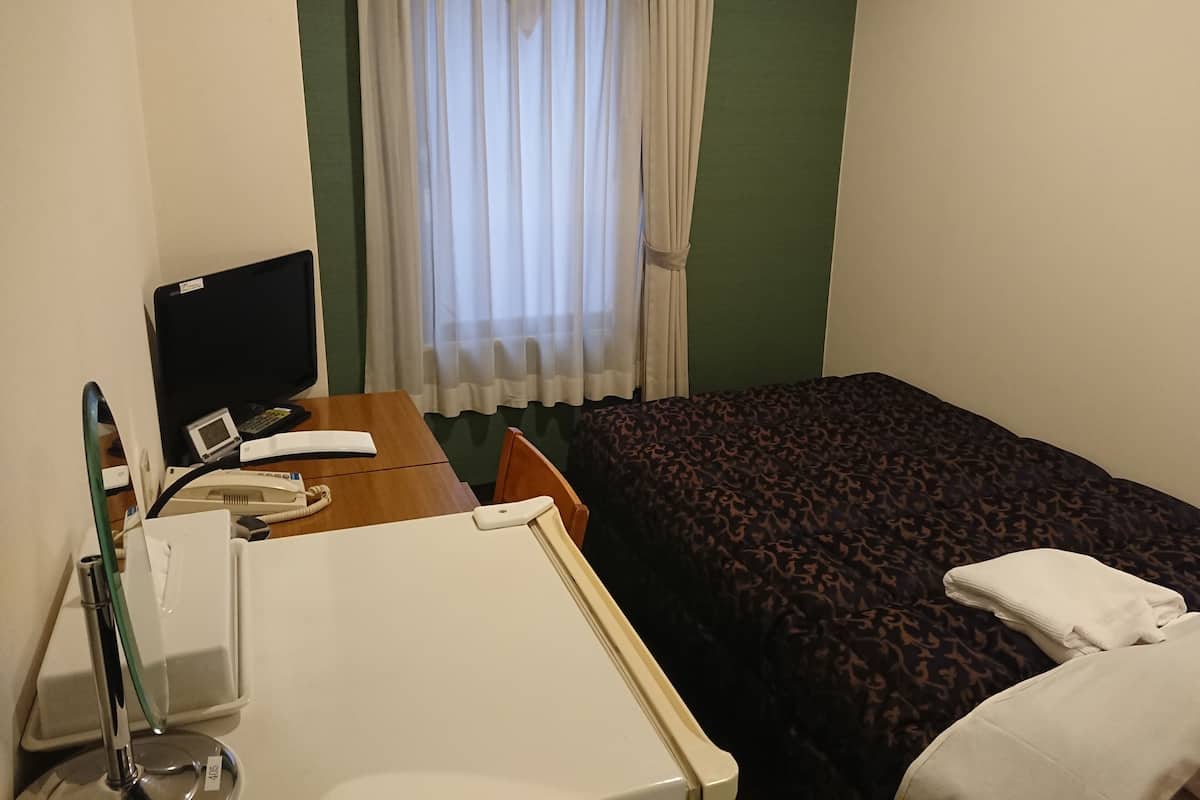 A hotel room with a bed, a desk with a computer, a telephone, and a bedside table.