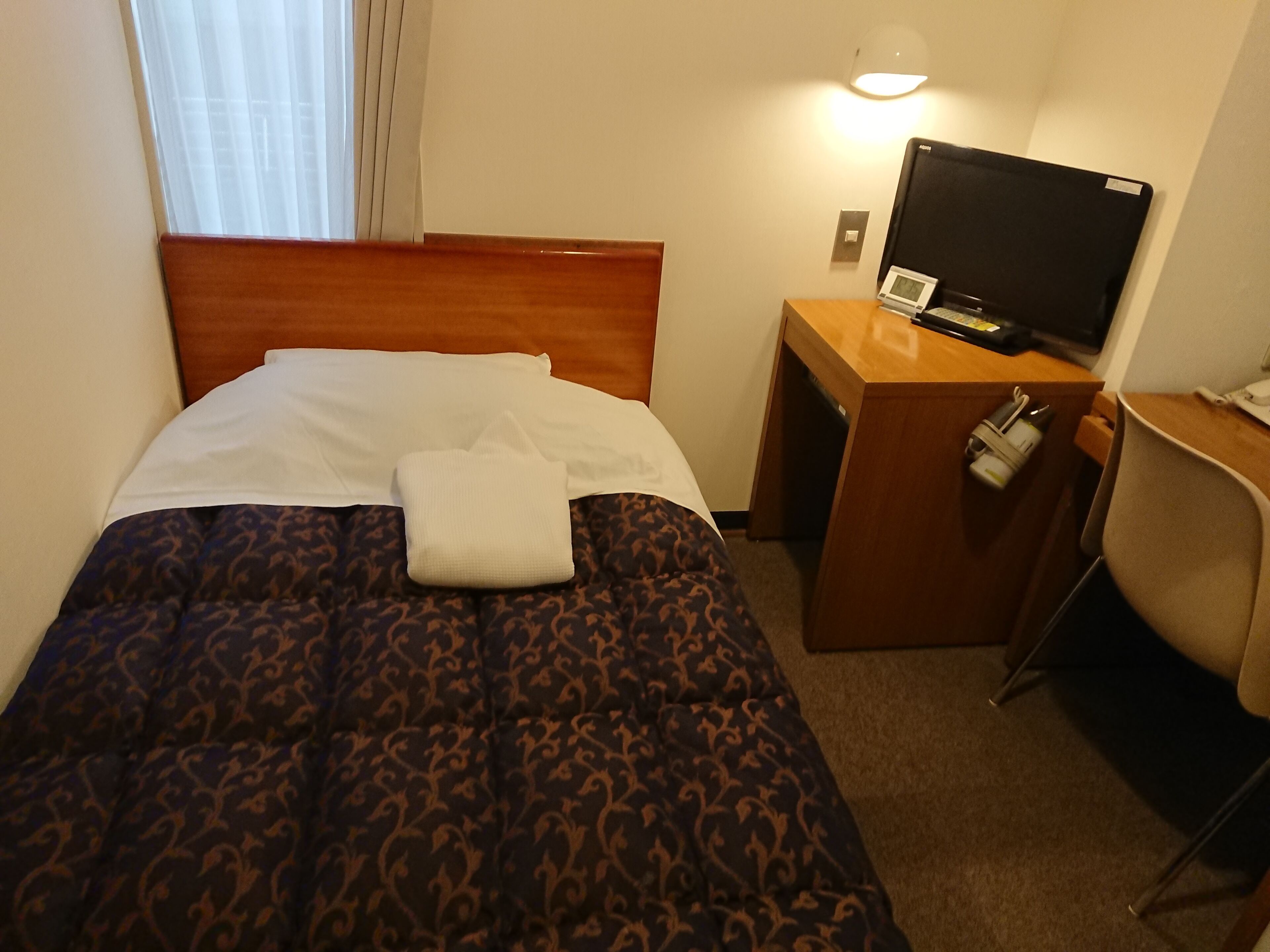 Una habitación de hotel con una cama, un escritorio con televisor y una silla.
