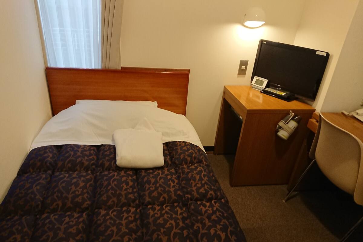 A hotel room with a bed, a desk with a television, and a chair.