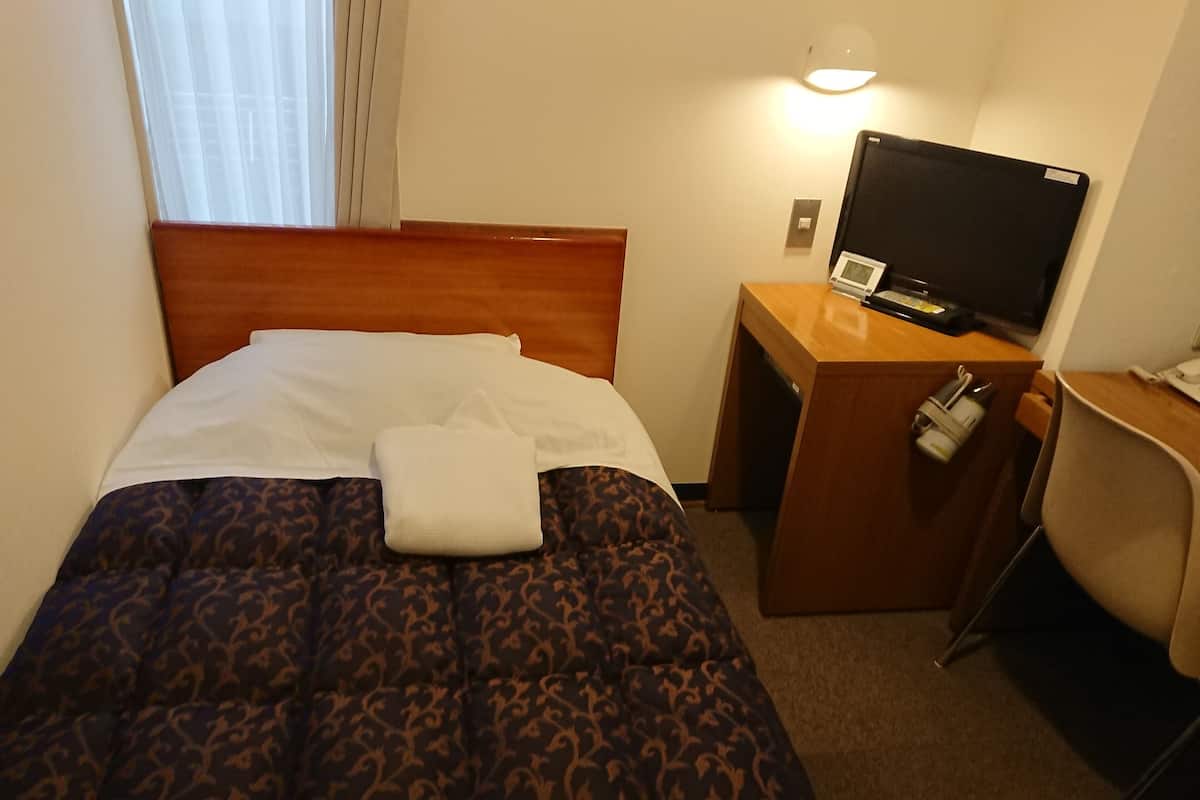 Una habitación de hotel con una cama, un escritorio con televisor y una silla.