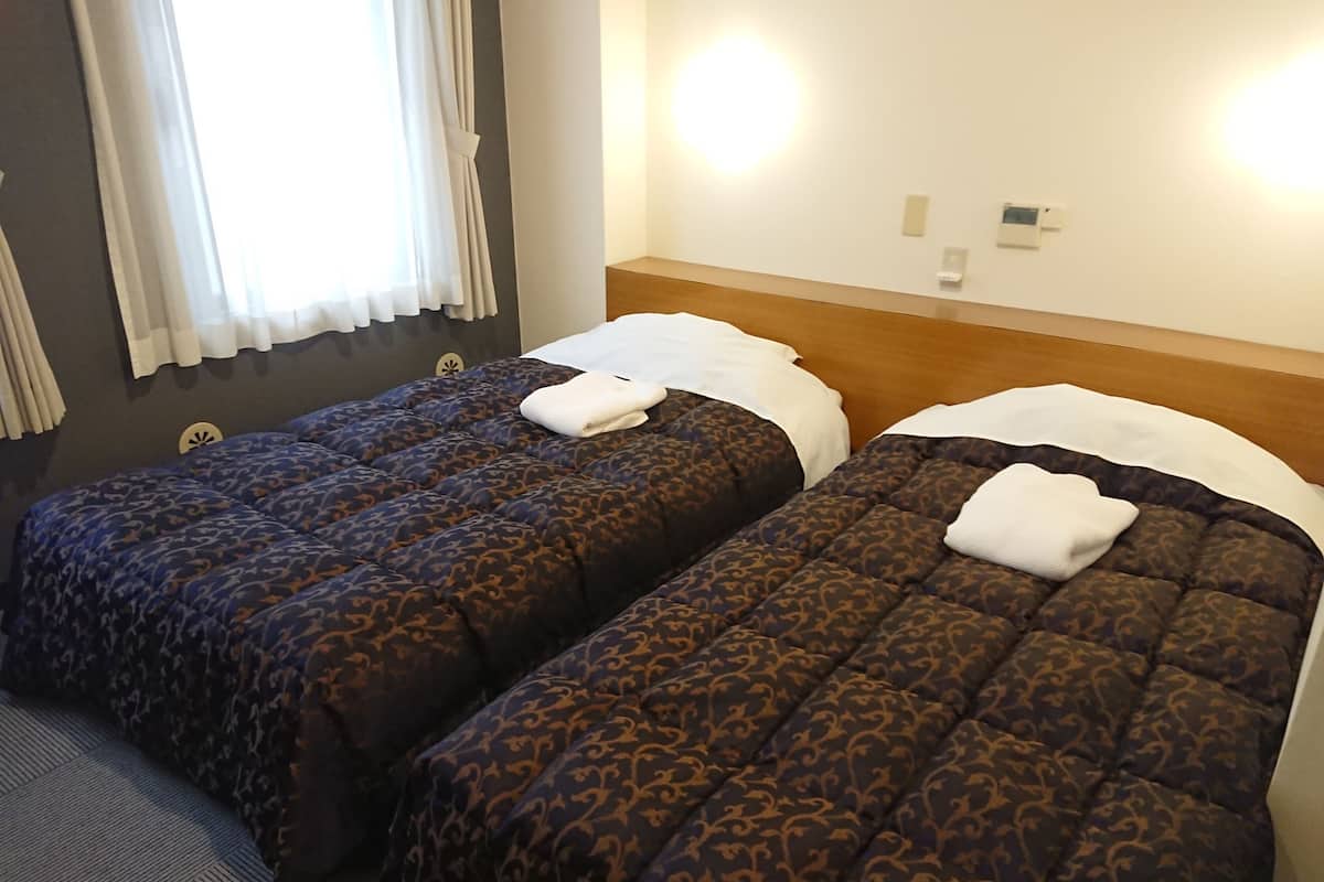 Two twin beds with patterned bedding, a window with curtains, and a wall-mounted light fixture.