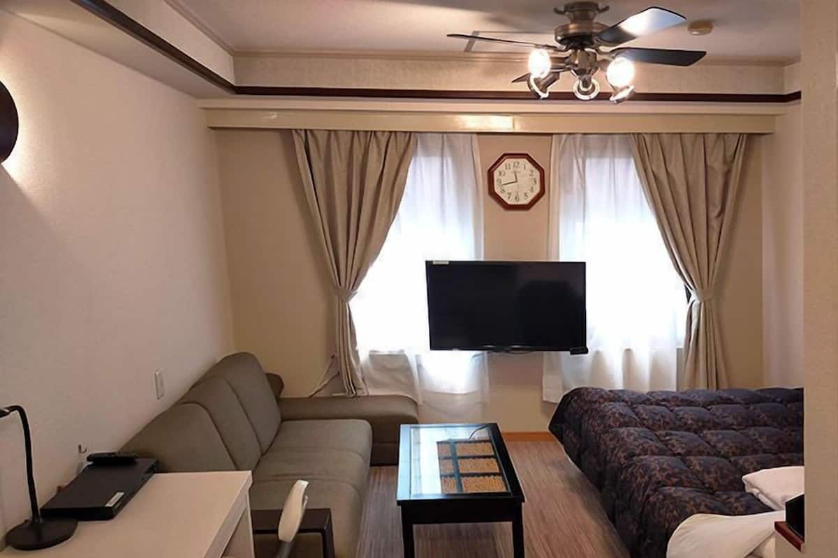 A hotel room with a sofa, a bed, a TV, a ceiling fan, and a clock on the wall.