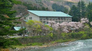 A building with a green roof, surrounded by cherry blossoms and a river. - Minakami Onsen Kkr Hotel Minakami Suimeiso (Minakami)