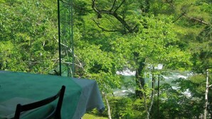 A table with a green tablecloth and a chair, set against a backdrop of dense green foliage and a river. - Minakami Onsen Kkr Hotel Minakami Suimeiso (Minakami)