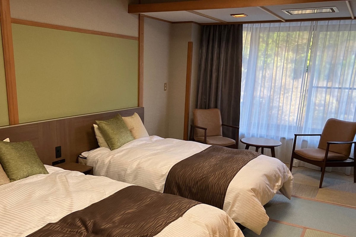 A hotel room with two beds, a small table, and a chair.