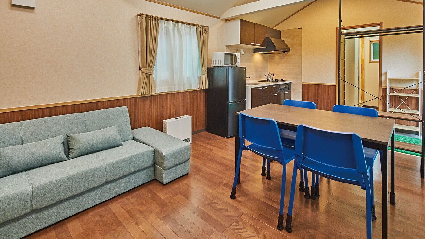 A compact living space with a sofa, dining table, chairs, a kitchenette, and a window with curtains.