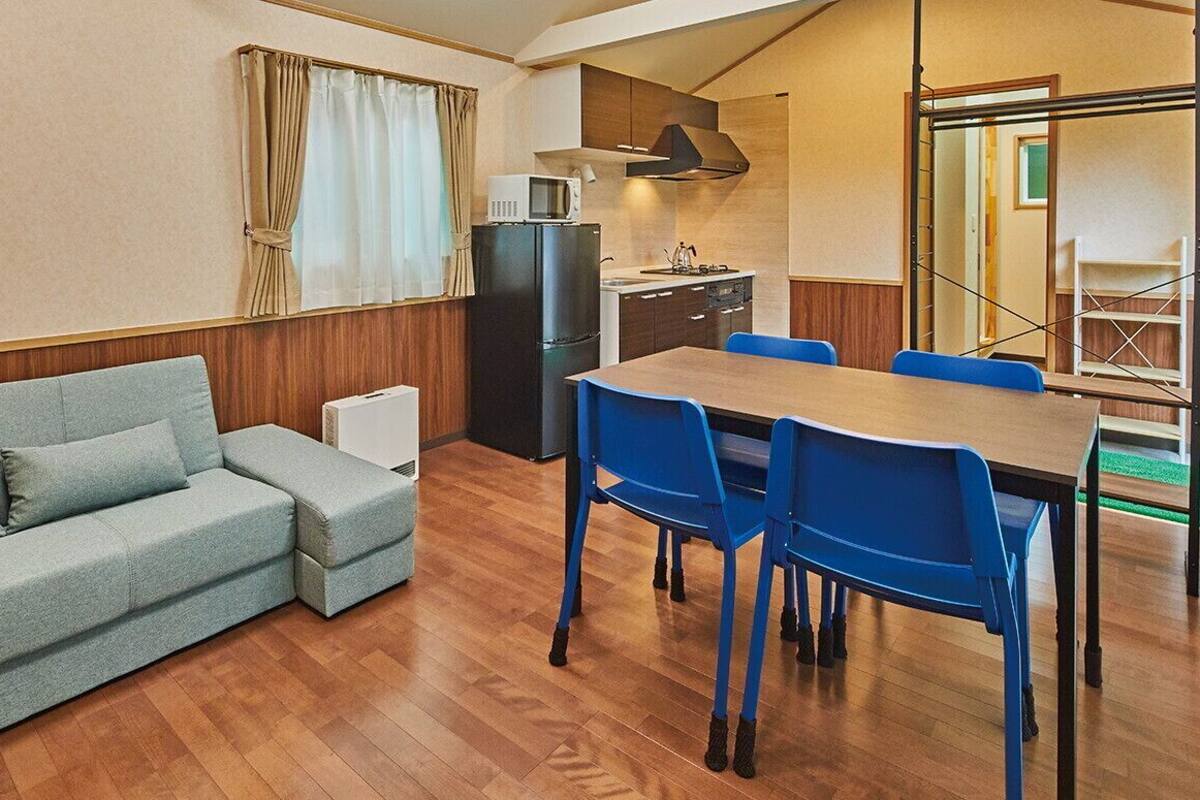 A compact living space with a sofa, dining table, chairs, a kitchenette, and a window with curtains.