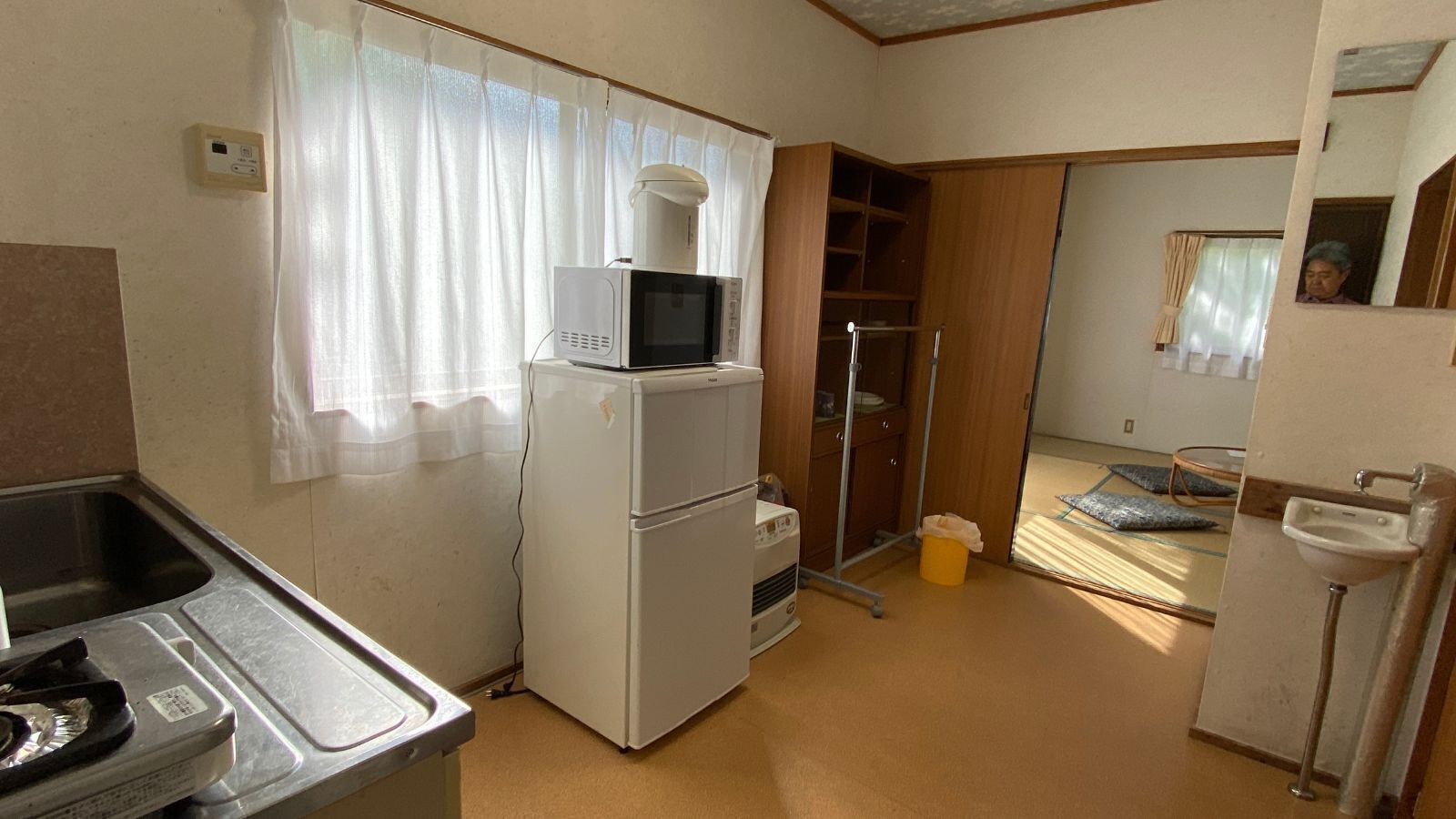 A compact kitchen with a refrigerator, microwave, sink, and a small window with curtains.