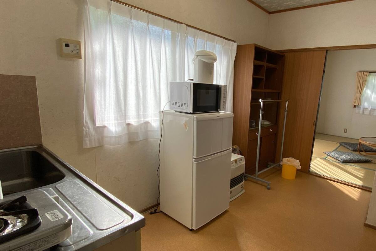 A compact kitchen with a refrigerator, microwave, sink, and a small window with curtains.