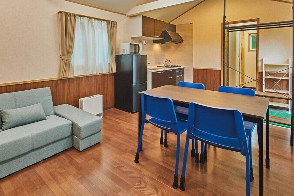 A compact living space with a sofa, dining table, chairs, a refrigerator, and a microwave.