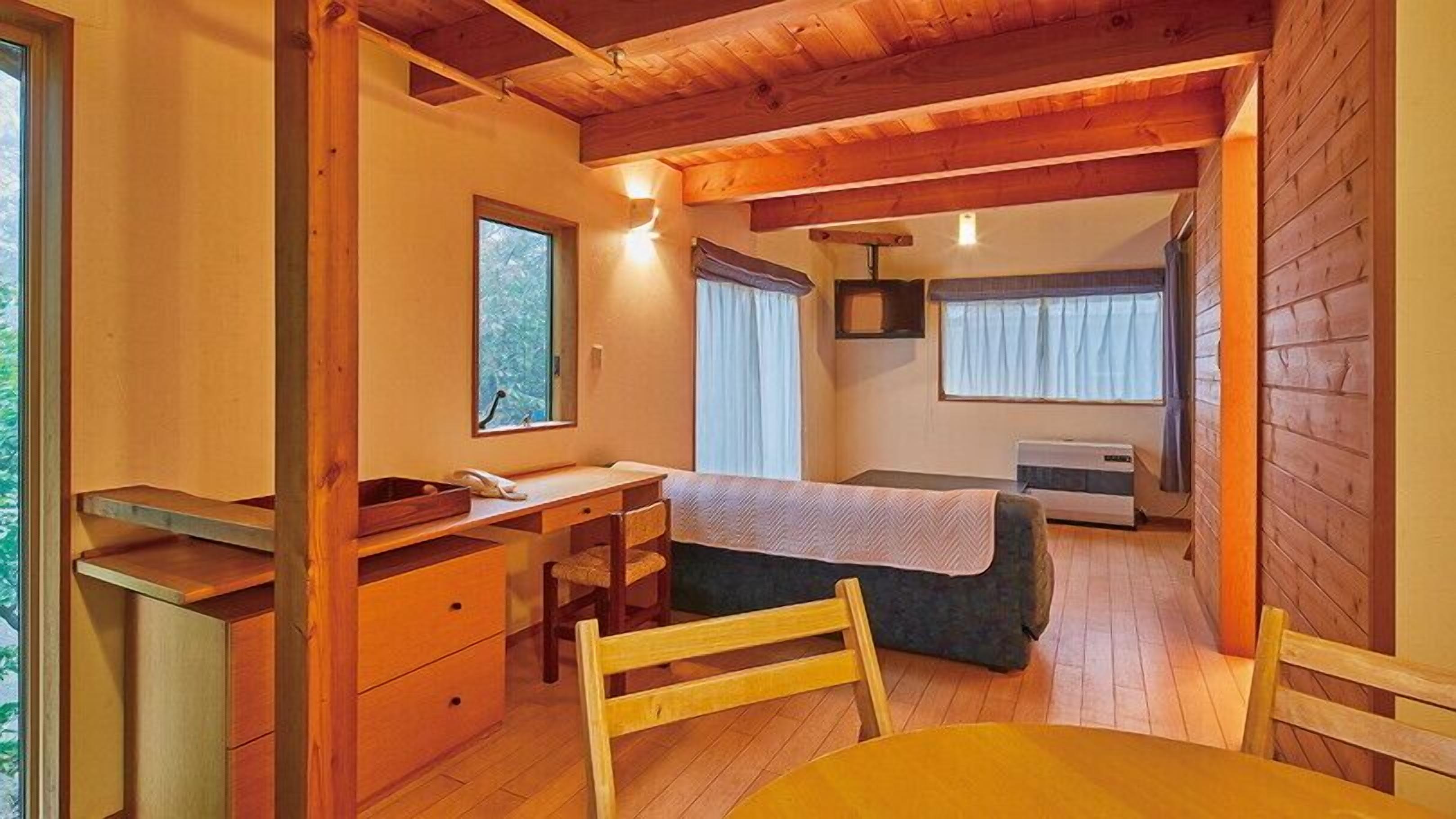 A compact room with a bed, a desk, a chair, a table, and a window.