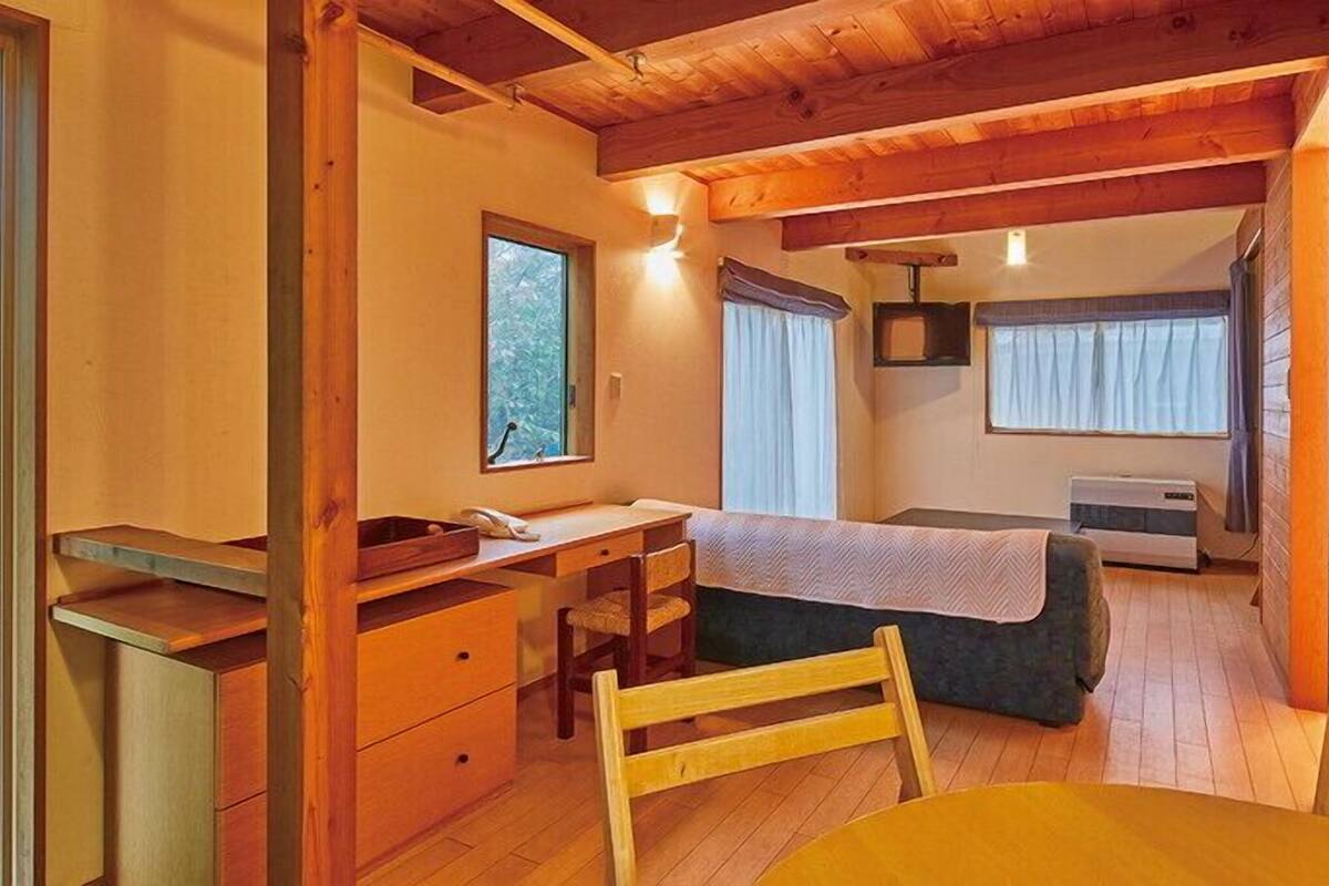 A compact room with a bed, a desk, a chair, a table, and a window.