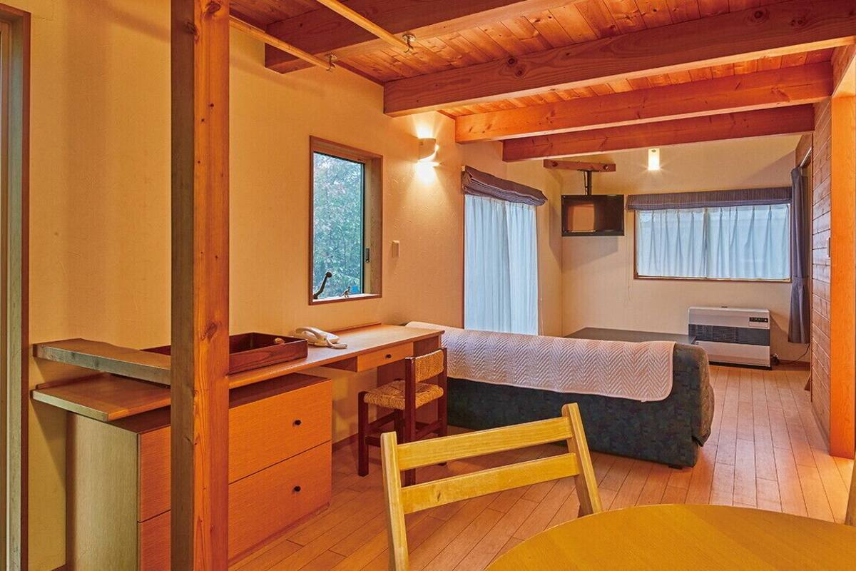 A room with a wooden desk, a bed, a chair, and a table.