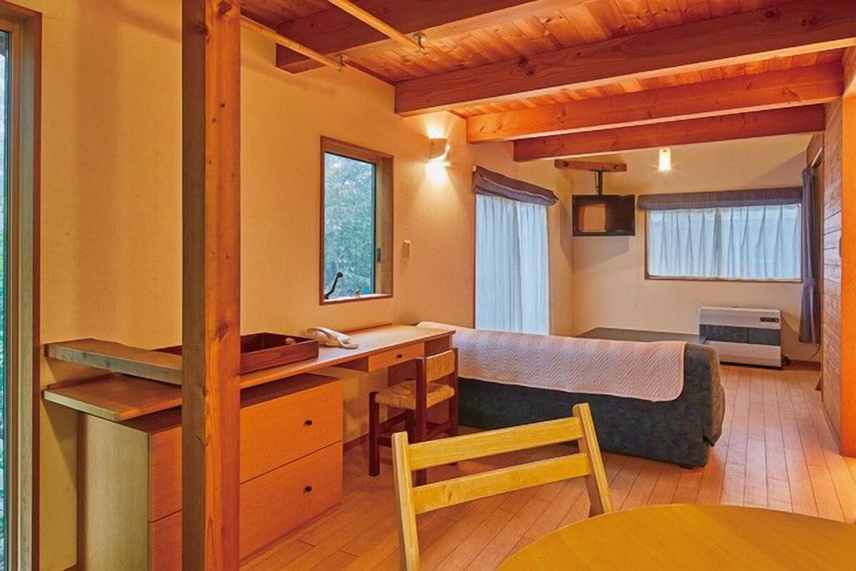 A compact room with a bed, a desk, a chair, a table, and a window.