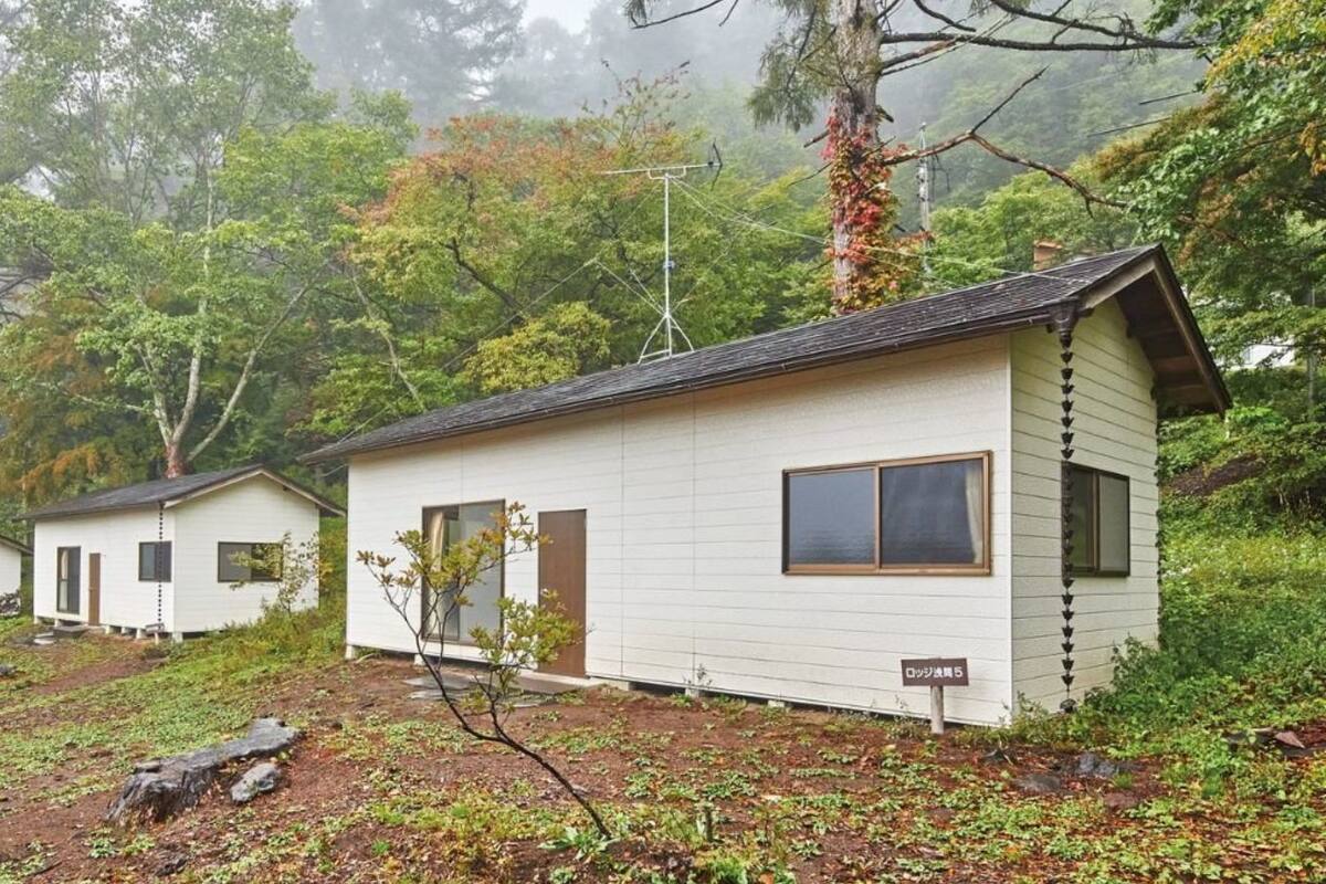 A row of small, white cabins with a single window and door, surrounded by dense forest and mist.