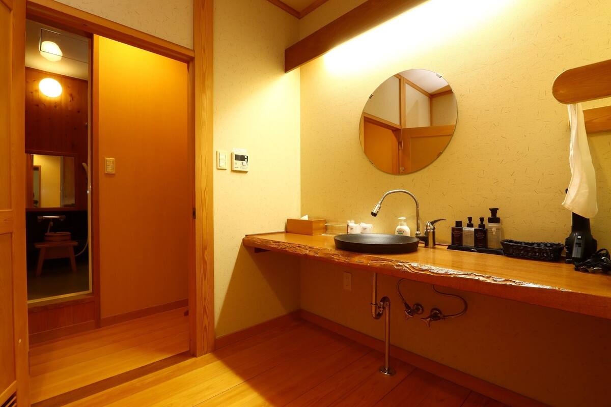 A bathroom with a wooden vanity, a round mirror, a sink, and toiletries.