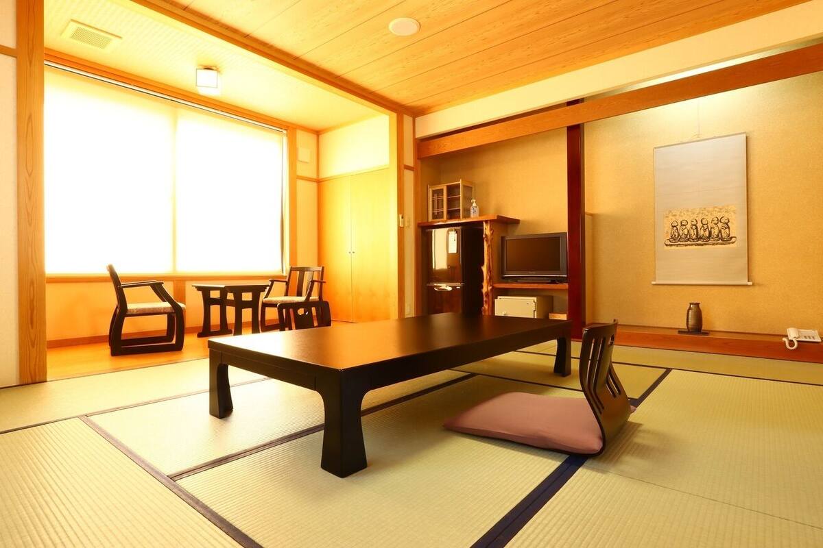 A traditional Japanese room with tatami flooring, a low table, chairs, a television, and a decorative piece on the wall.