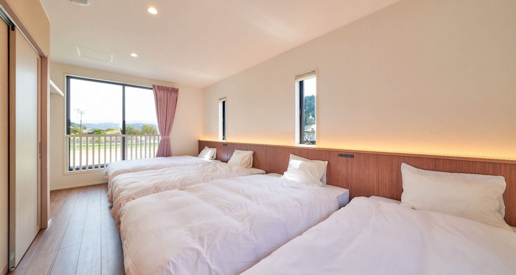 A hotel room with two beds, large windows, and a balcony.