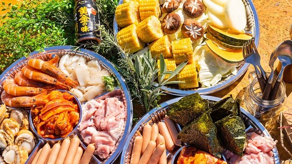 A variety of food items including corn, sausages, and seafood, arranged on a table outdoors.