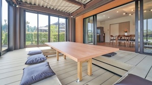 Interior moderno com mesa de jantar de madeira, assentos acolchoados, grandes portas de vidro deslizantes e vista para o verde lá fora.