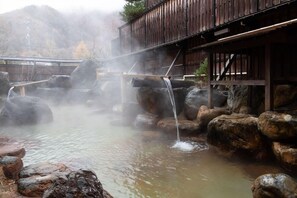 Un balneario tradicional de madera con múltiples aguas termales, rodeado de rocas y una estructura de madera en lo alto.