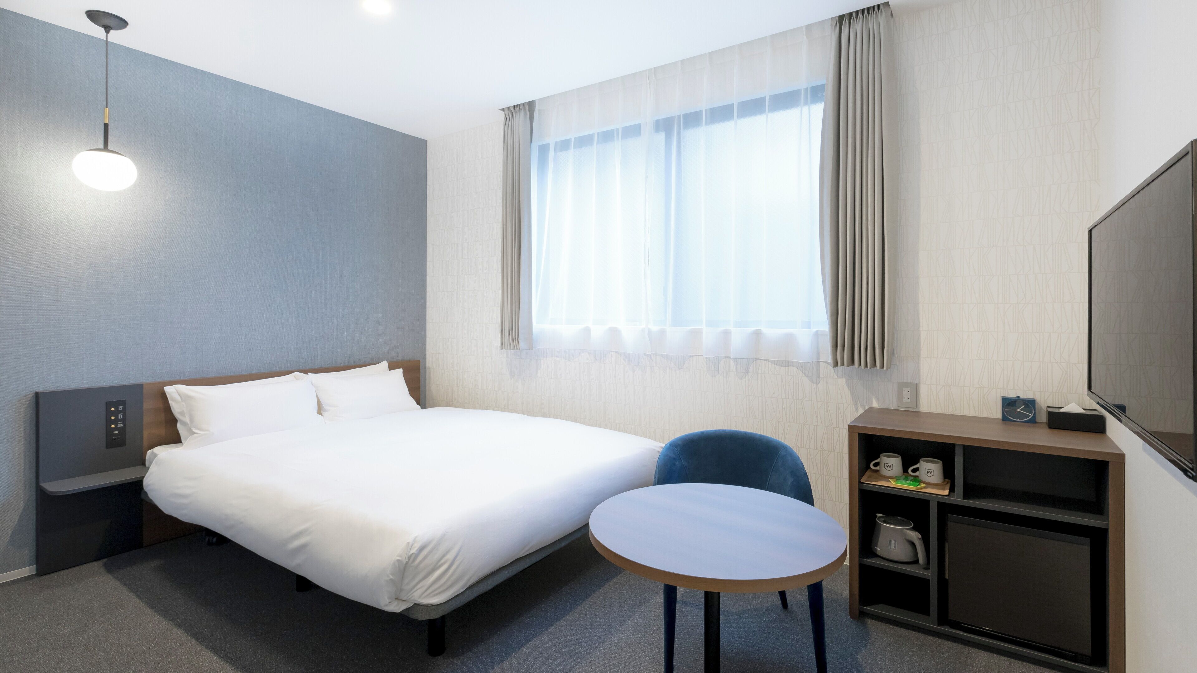 Ein Hotelzimmer mit Bett, Nachttisch, Stuhl, Fernseher und einem Fenster mit Vorhängen.