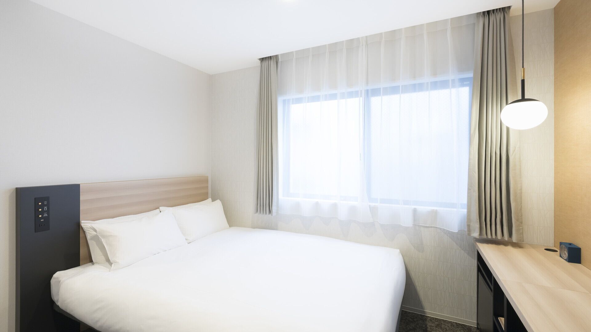 Une chambre d’hôtel avec un lit, un panneau de commande, un bureau et une fenêtre avec des rideaux.
