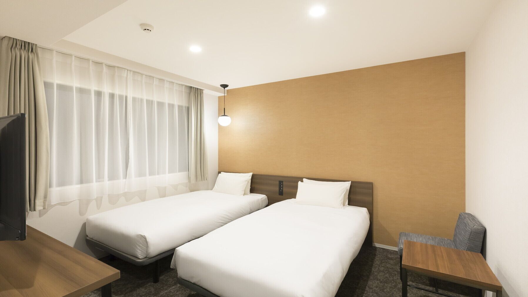 Une chambre d’hôtel avec deux lits simples, un bureau, une chaise et un téléviseur.