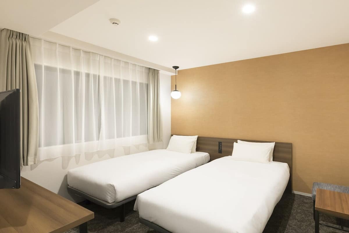 A hotel room with two single beds, a desk, a chair, and a television.