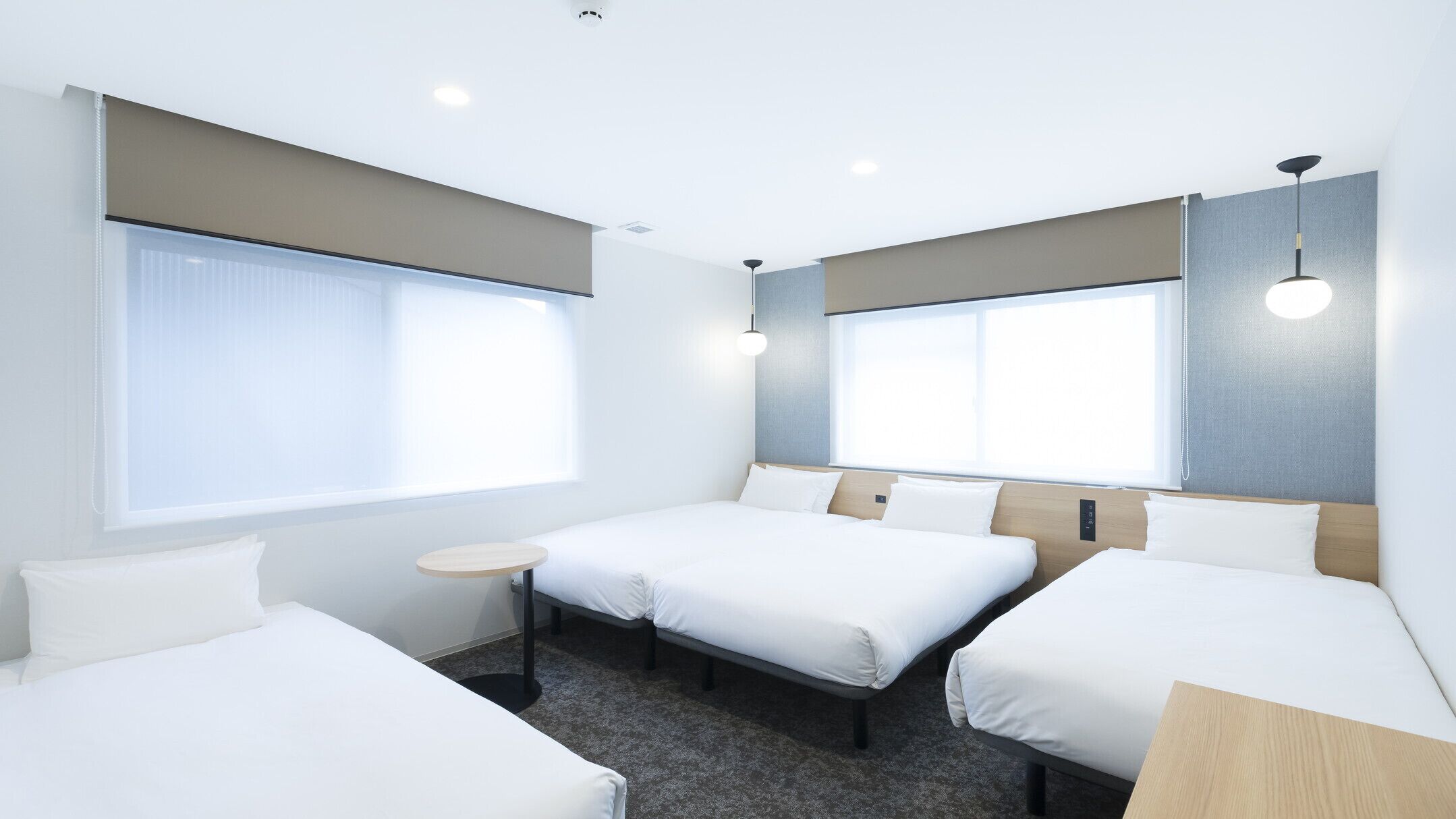Une chambre d’hôtel avec deux lits simples, une petite table ronde et de grandes fenêtres.