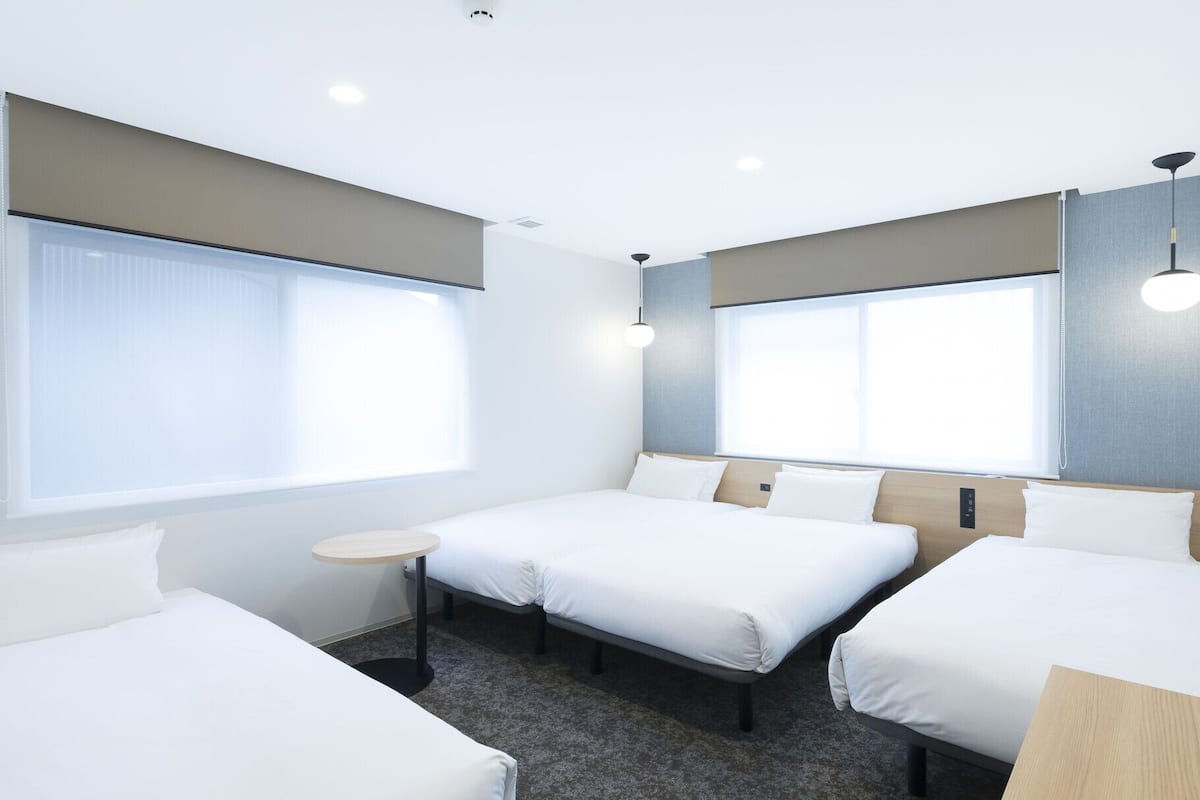A hotel room with two single beds, a small round table, and large windows.