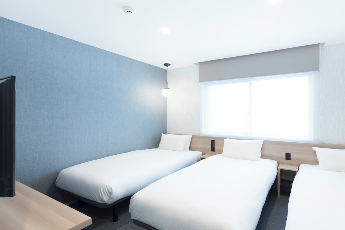 A hotel room with two single beds, a large window, and a modern design.
