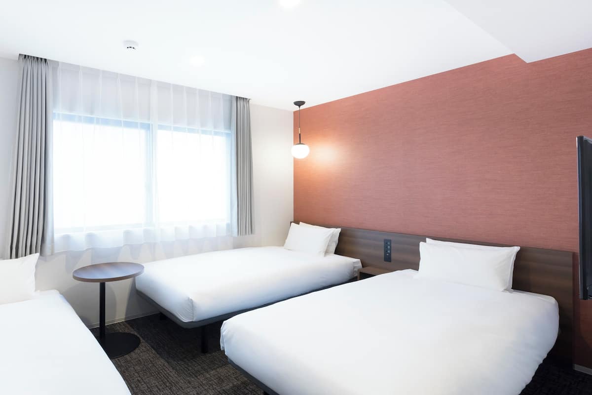 A hotel room with two beds, a small table, a TV, and a window with curtains.
