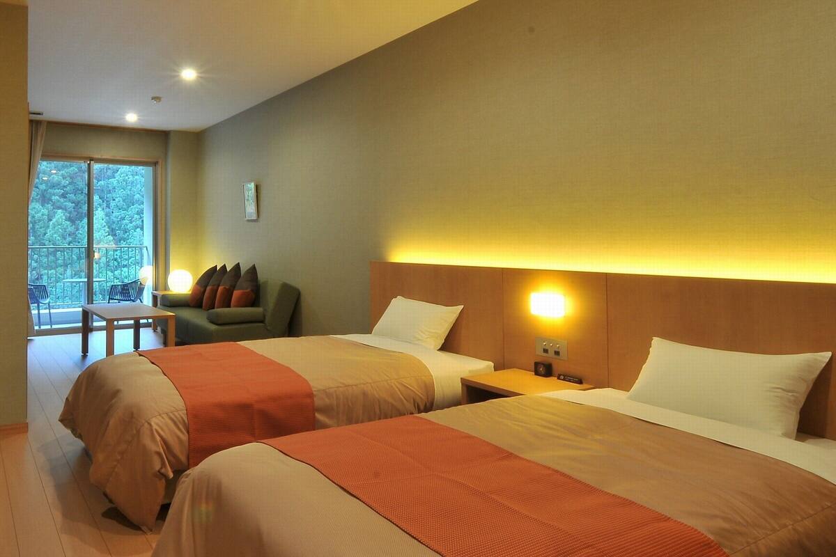 A hotel room with two beds, a balcony with a view, a small table, and a sofa.