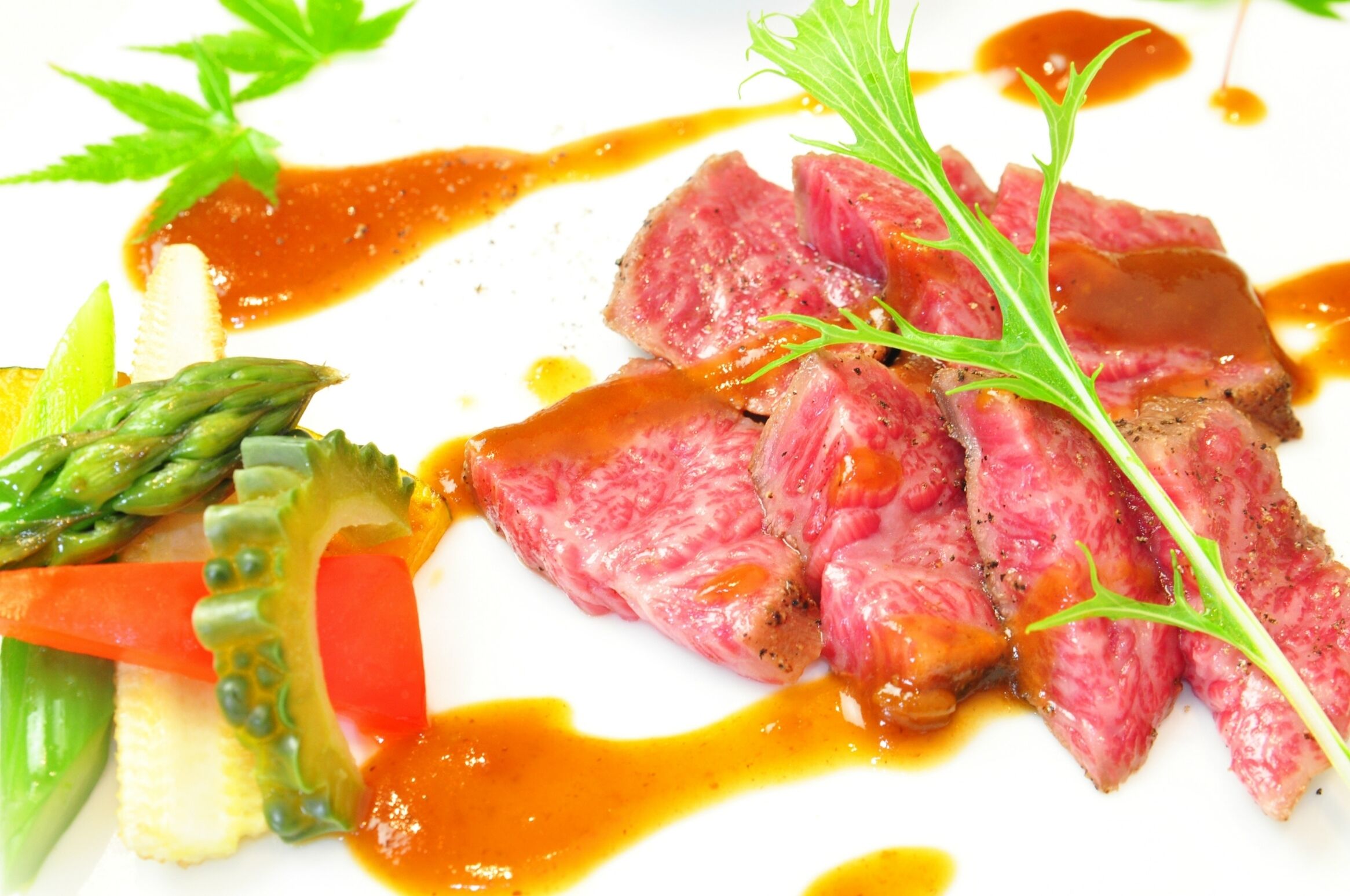 A dish with steak, asparagus, and vegetables on a white plate.