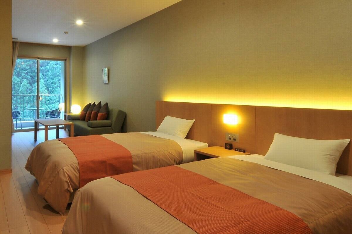 A hotel room with two beds, a balcony, a sofa, and a table.