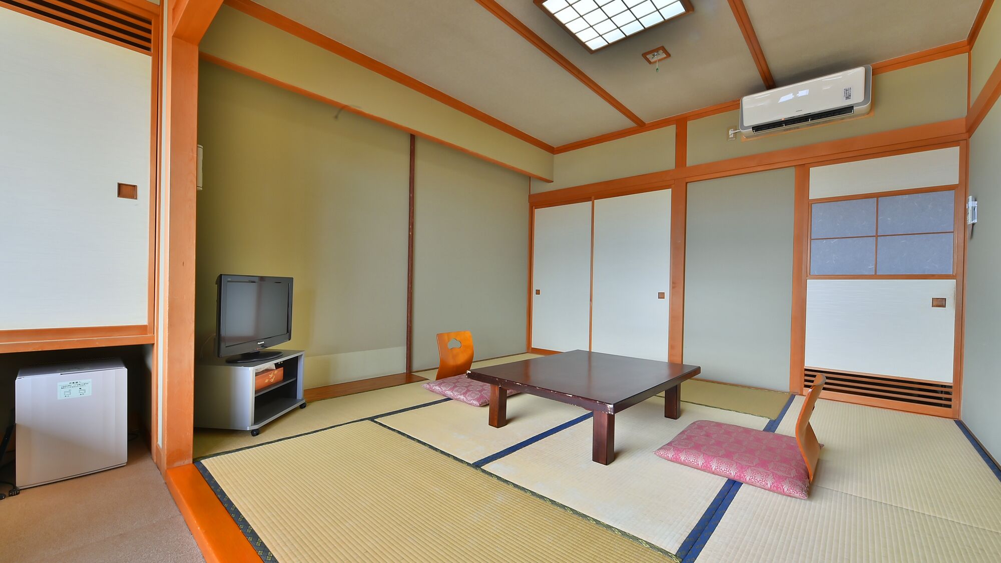 Ein traditioneller japanischer Raum mit Tatami-Boden, einem Fernseher, einem kleinen Kühlschrank und einer Schiebetür.