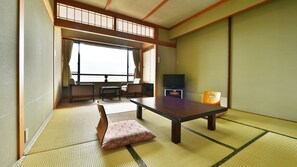 Una habitación japonesa tradicional con suelo de tatami, una mesa baja, sillas, un televisor y una puerta corredera.
