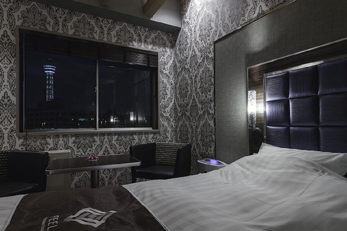 Habitación de hotel con una cama grande, un escritorio con silla, una ventana con vistas a una torre y papel tapiz estampado.