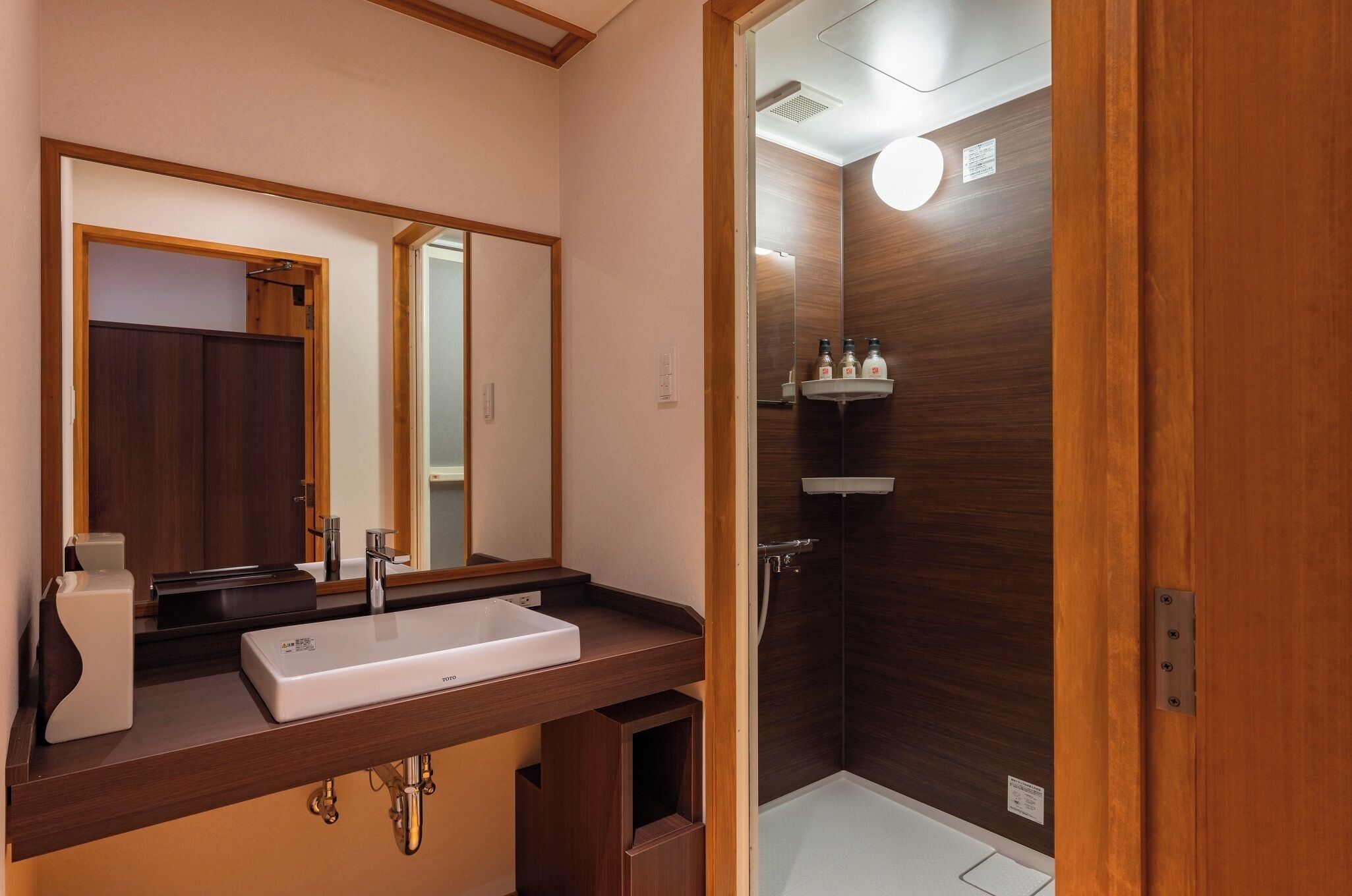 A bathroom with a wooden vanity, a sink, a mirror, and a shower area.